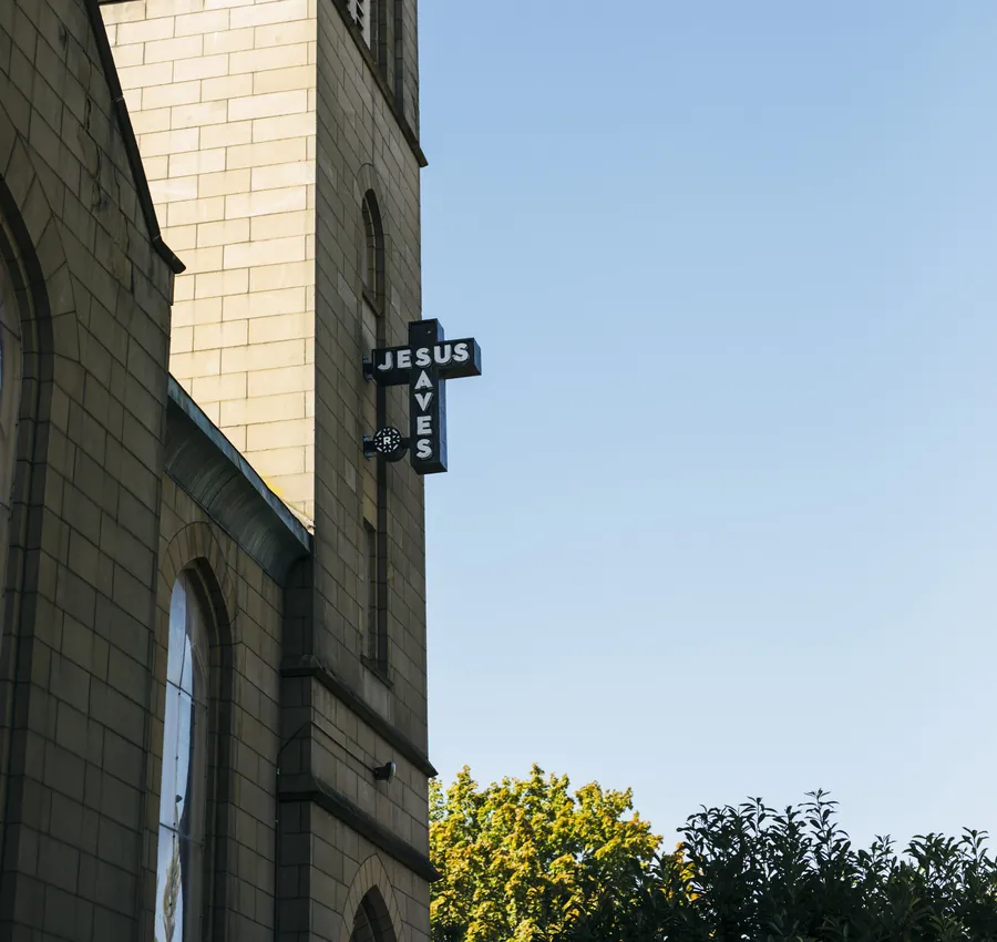 A stone church tower with a Jesus Saves sign against a clear sky