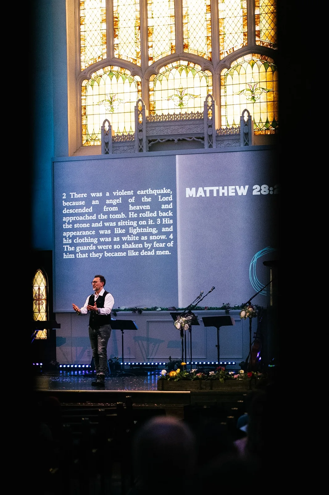 Bubba Jennings preaching beneath the stained-glass windows of Resurrection Church, with Matthew 28:2-4 on the screen